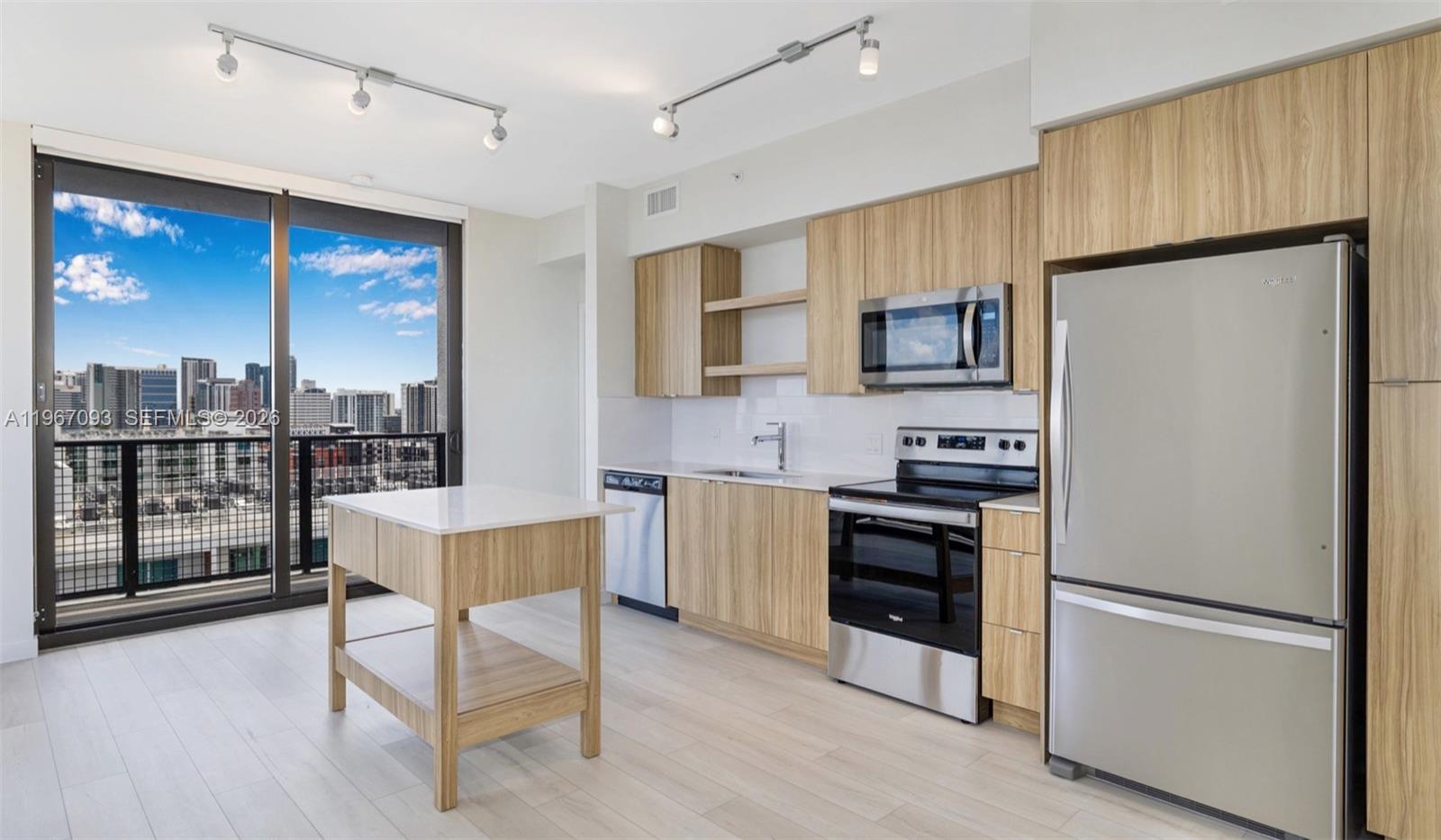A modern kitchen features light wood cabinetry, stainless steel appliances, a center island, and balcony views — FORT LAUDERDALE, FL