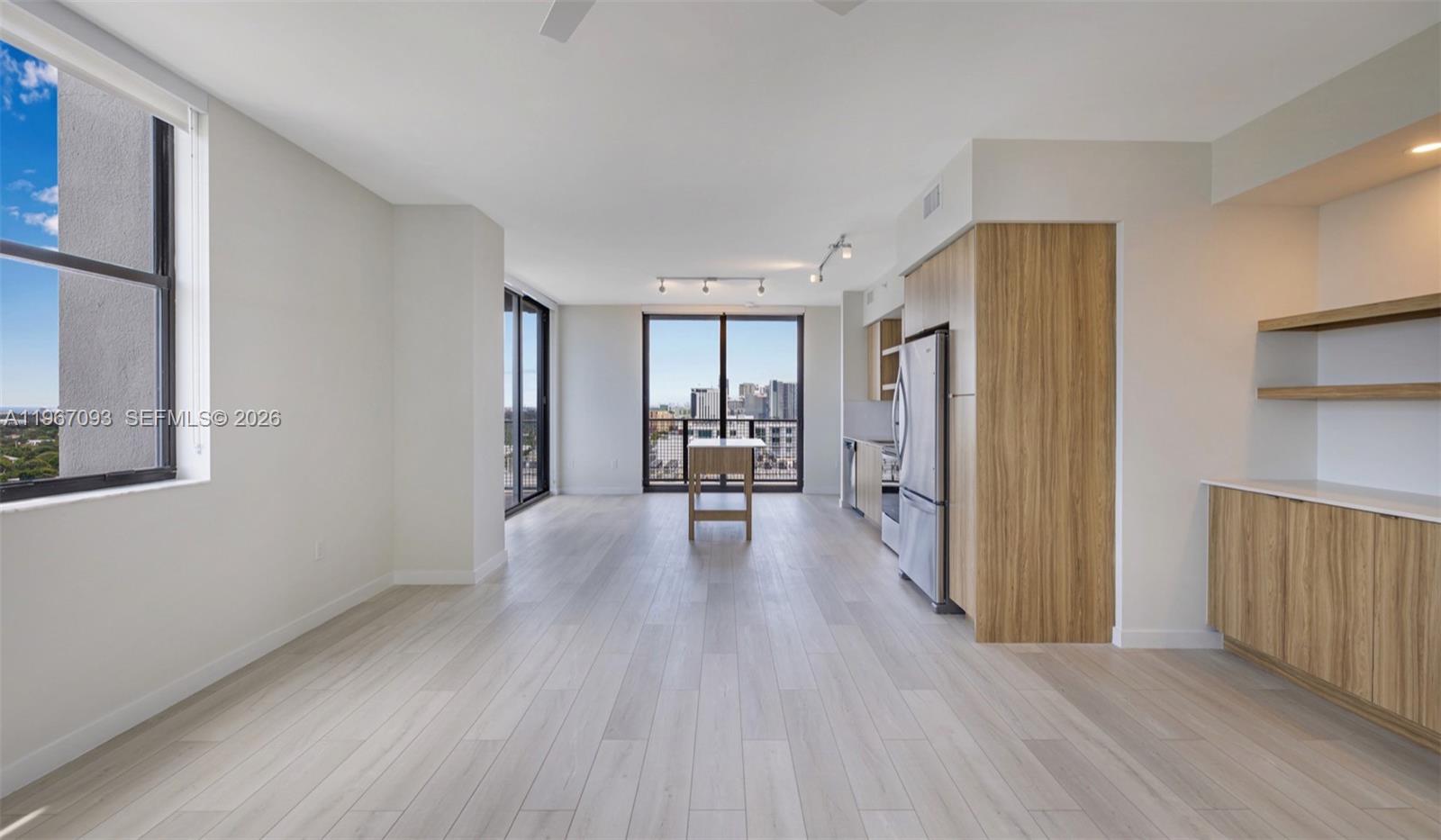 A modern kitchen and living area features light wood cabinetry, stainless appliances, and balcony views — FORT LAUDERDALE, FL