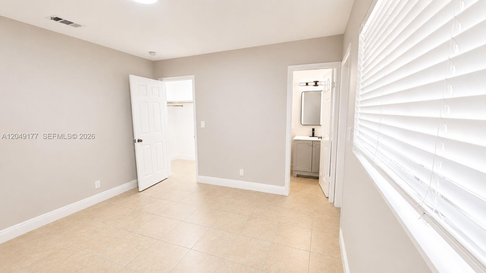 A bedroom with beige tile flooring, a walk-in closet, and an attached bathroom — 2332 Roosevelt St # 32, Hollywood FL 33020, HOLLYWOOD, FL