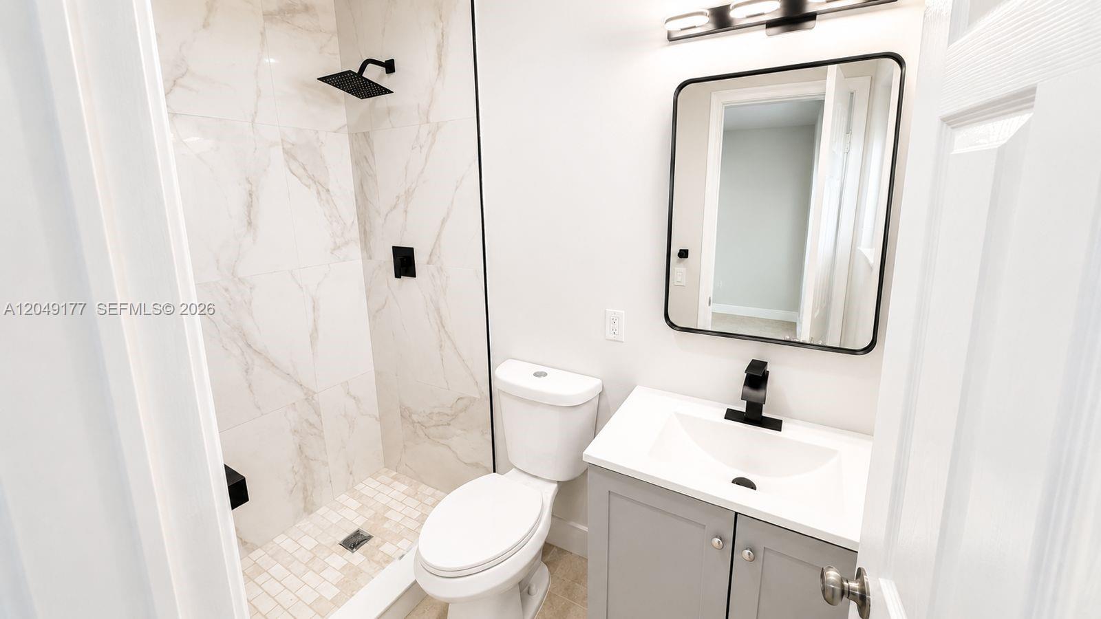 A modern bathroom features a walk-in shower with marble-look tile, a vanity, and toilet — 2332 Roosevelt St # 32, Hollywood FL 33020, HOLLYWOOD, FL