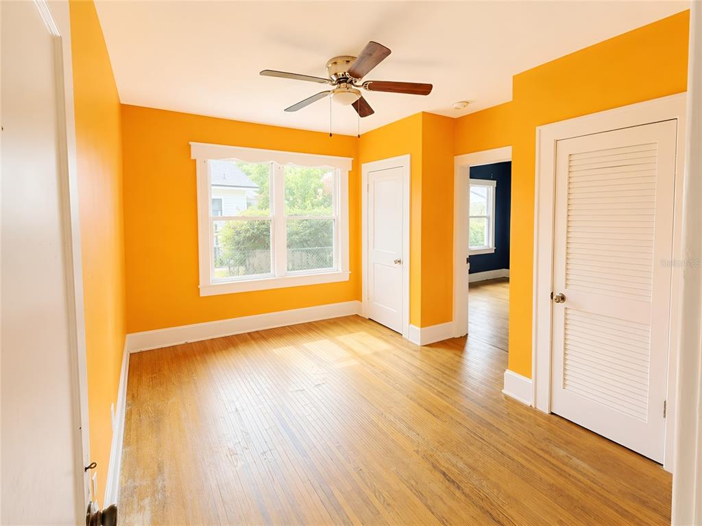 An empty bedroom with orange walls, hardwood floors, a ceiling fan, and white trim — 1037 LEXINGTON STREET, LAKELAND, FL