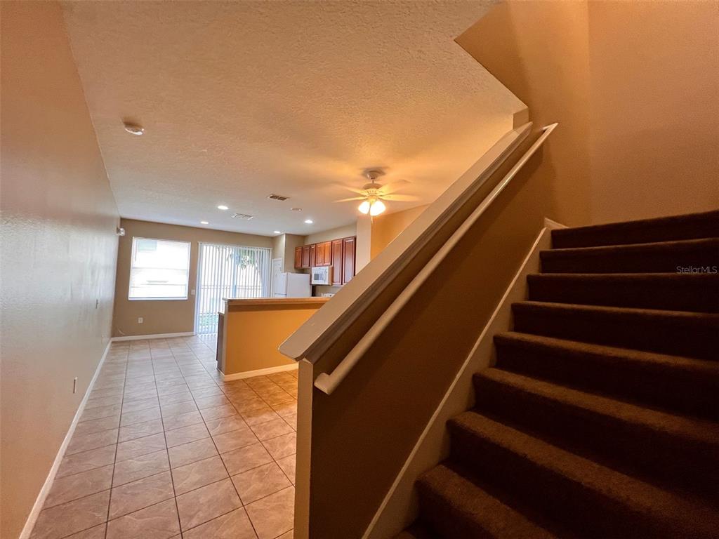A view from a carpeted staircase looking toward a tiled kitchen and living area — 7602 LONG ISLAND DRIVE, KISSIMMEE, FL