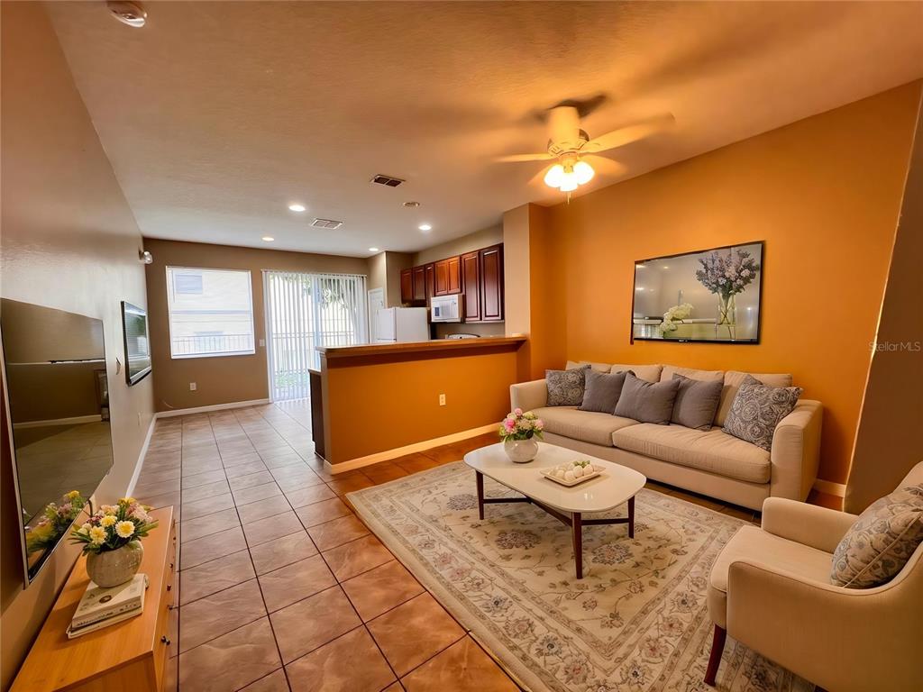 A living room with tile floors, a beige sofa, and an open kitchen with dark cabinets — 7602 LONG ISLAND DRIVE, KISSIMMEE, FL