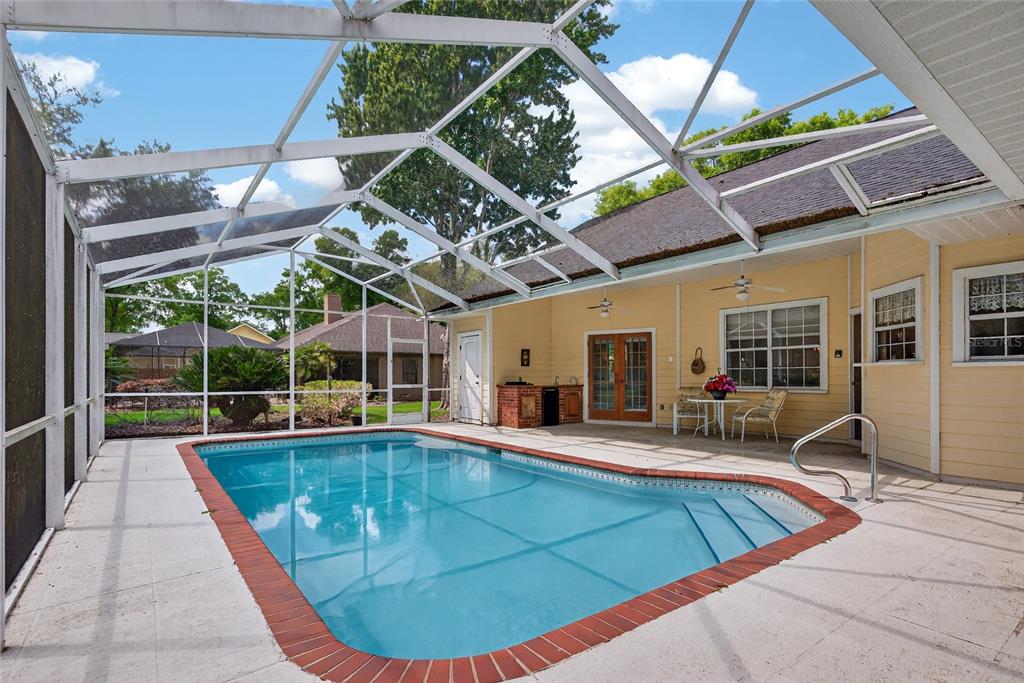 A screened-in swimming pool with a brick border sits on a patio next to a house — 5174 NE 7TH PLACE, OCALA, FL