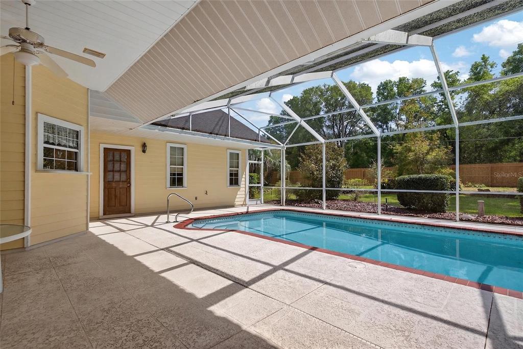 A screened-in patio features a swimming pool, concrete decking, and yellow exterior house walls — 5174 NE 7TH PLACE, OCALA, FL
