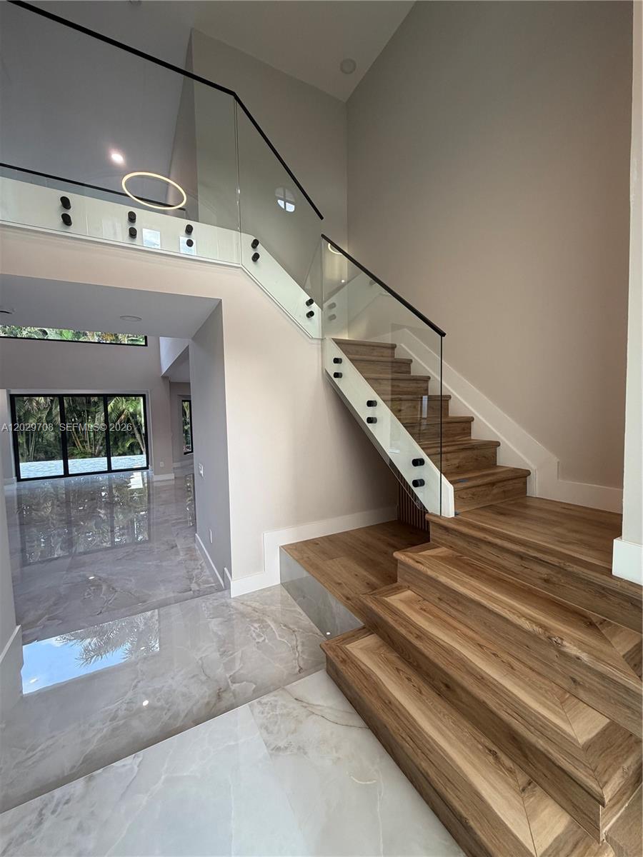 A modern foyer features a glass-railed wooden staircase and polished marble flooring — 4499 NW 93rd Doral Ct, Doral FL 33178, DORAL, FL
