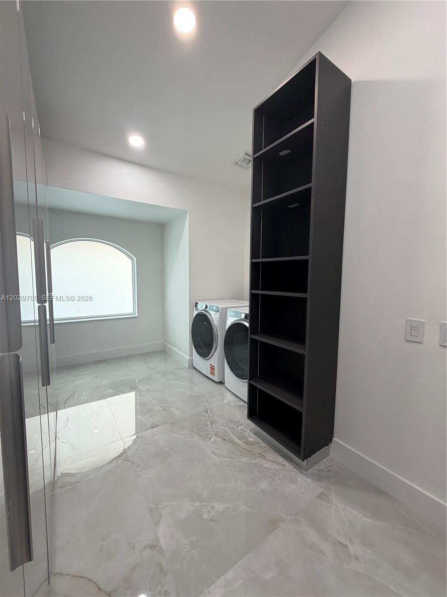 A laundry room features white walls, marble-look tile flooring, a tall shelving unit, and appliances — 4499 NW 93rd Doral Ct, Doral FL 33178, DORAL, FL