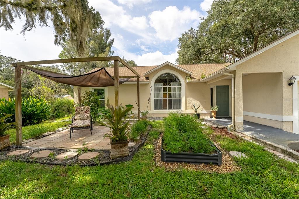 A backyard features a paved patio with a shade sail, a raised garden bed, and landscaping — 6449 ADAM STREET, ST CLOUD, FL