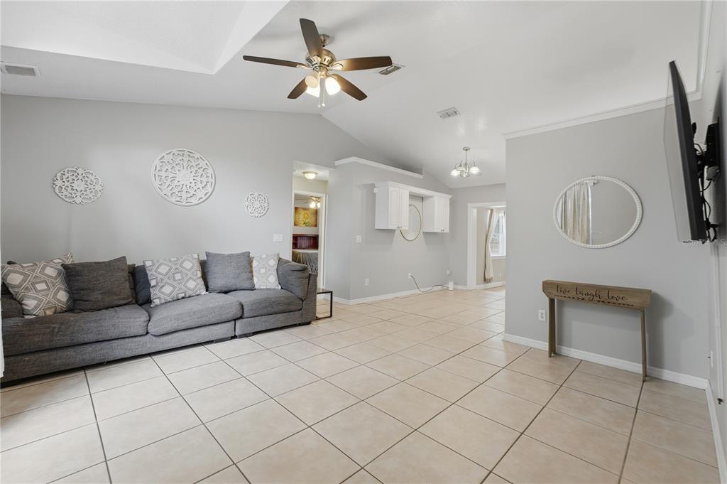 A living room with light gray walls, tile flooring, a gray sofa, and vaulted ceilings — 6449 ADAM STREET, ST CLOUD, FL