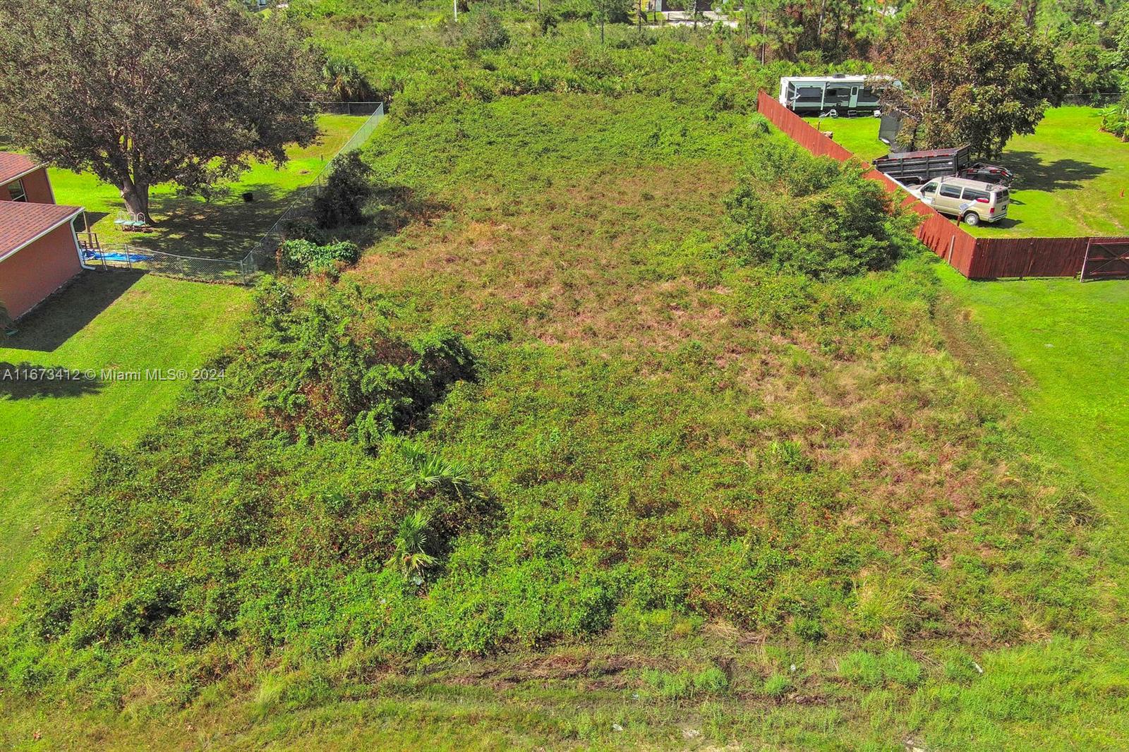 An aerial view shows a vacant, overgrown rectangular lot bordered by fences and neighboring properties — 1413 5th Ave, Lehigh Acres FL 33972, LEHIGH ACRES, FL