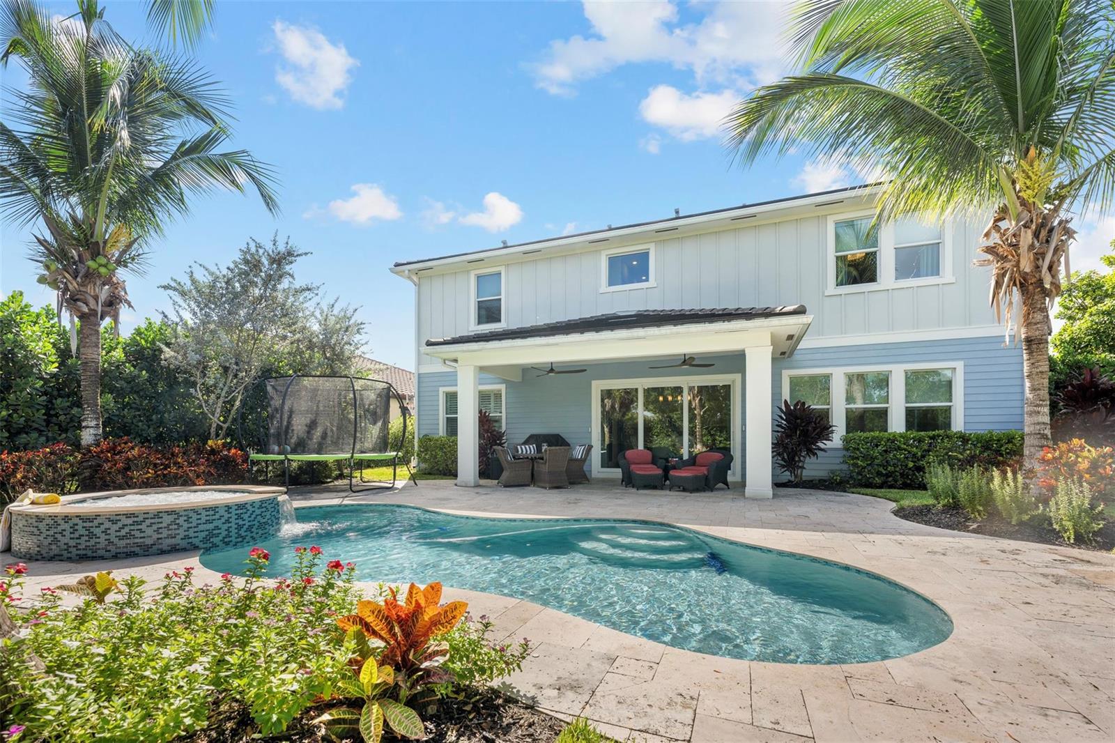 A two-story house with a backyard pool, spa, patio, and trampoline under a blue sky — 1018 Sweetgrass Street, Loxahatchee FL 33470, LOXAHATCHEE, FL