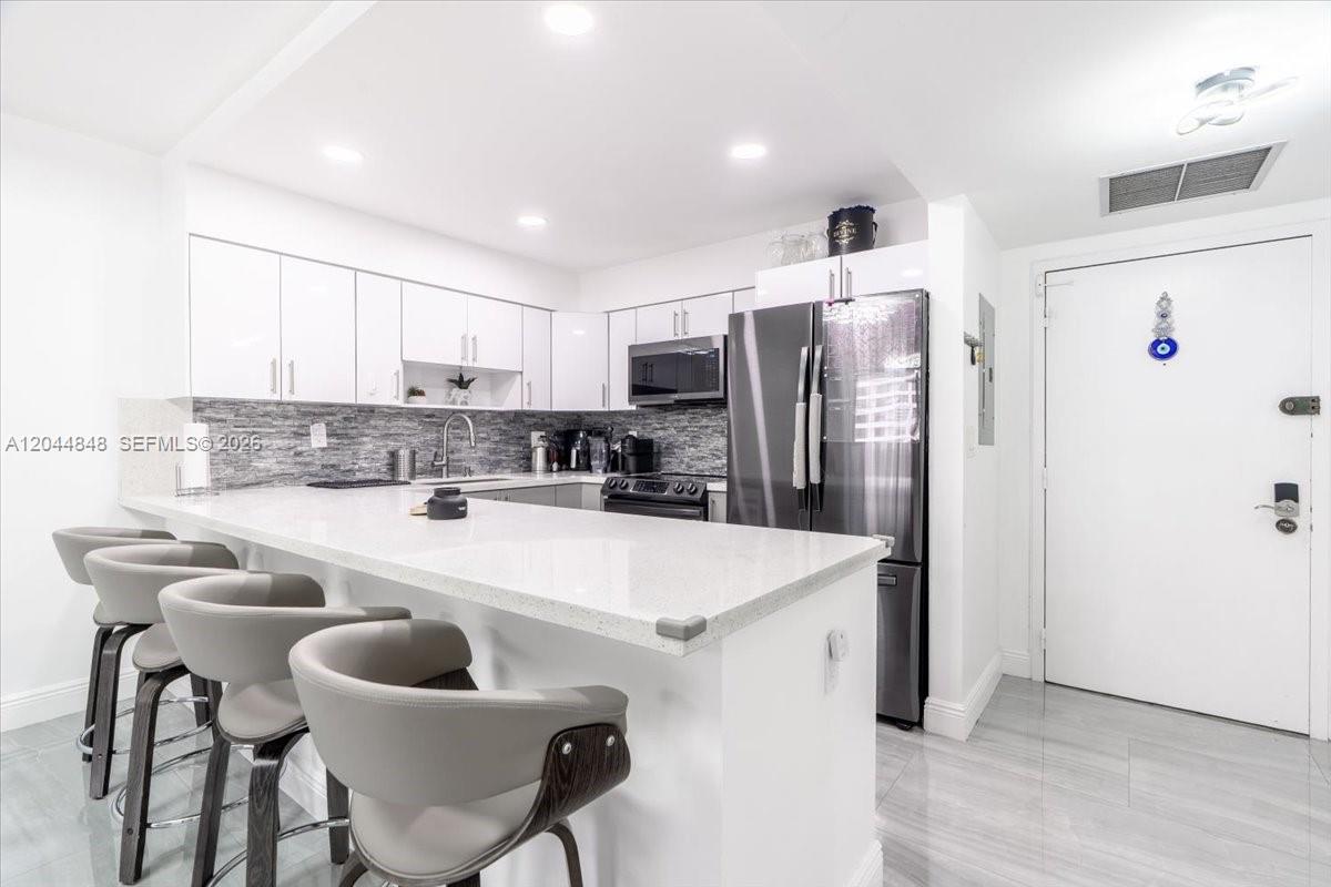 A modern kitchen features white cabinetry, a quartz countertop island, and stainless steel appliances — 600 Three Islands Blvd # 1413, Hallandale Beach FL 33009, HALLANDALE BEACH, FL