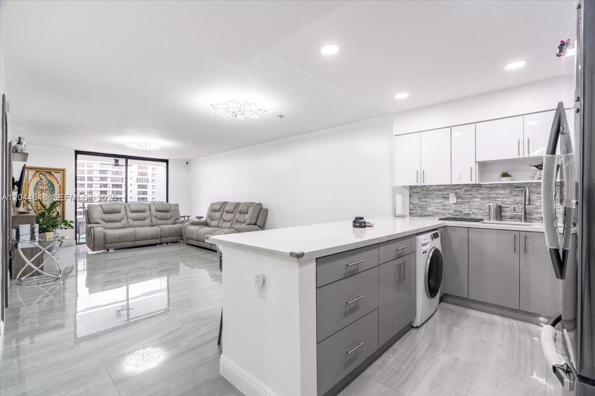 A modern kitchen with gray lower cabinets and white upper cabinets opens to a living area — 600 Three Islands Blvd # 1413, Hallandale Beach FL 33009, HALLANDALE BEACH, FL