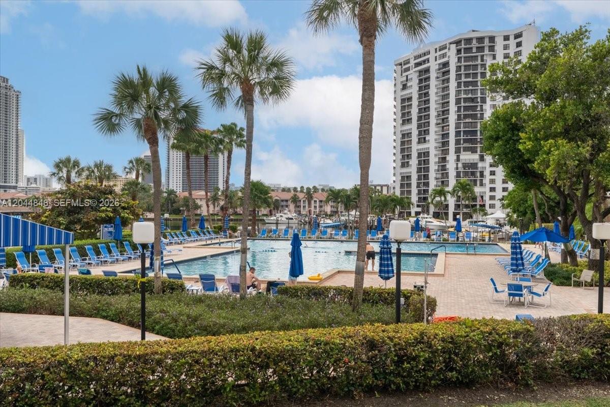 A swimming pool area with lounge chairs, palm trees, and high-rise buildings in the background — 600 Three Islands Blvd # 1413, Hallandale Beach FL 33009, HALLANDALE BEACH, FL