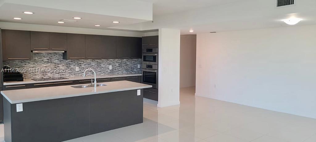 A modern kitchen features dark cabinetry, a large island, and light-colored countertops — 7751 NW 107th Ave # 504, Doral FL 33178, DORAL, FL