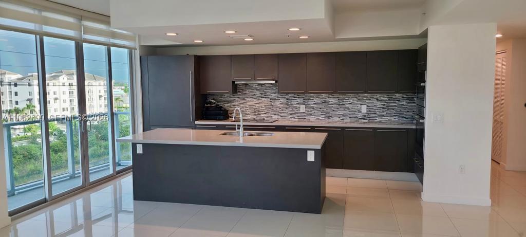 A modern kitchen features dark cabinetry, a large island with a sink, and tile flooring — 7751 NW 107th Ave # 504, Doral FL 33178, DORAL, FL