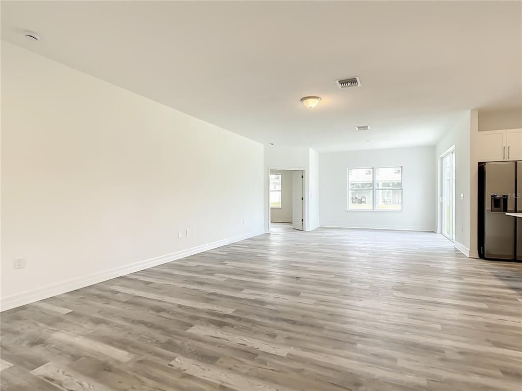 An open-concept living area features light wood-look flooring, white walls, and a stainless steel refrigerator — 14210 LUXO AVENUE, PORT CHARLOTTE, FL