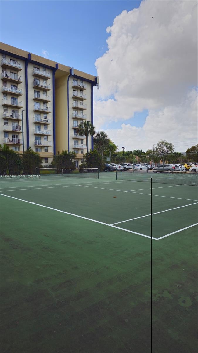 A tennis court sits in front of a multi-story residential building under a cloudy sky — 4550 NW 9th St # 505E, Miami FL 33126, MIAMI, FL