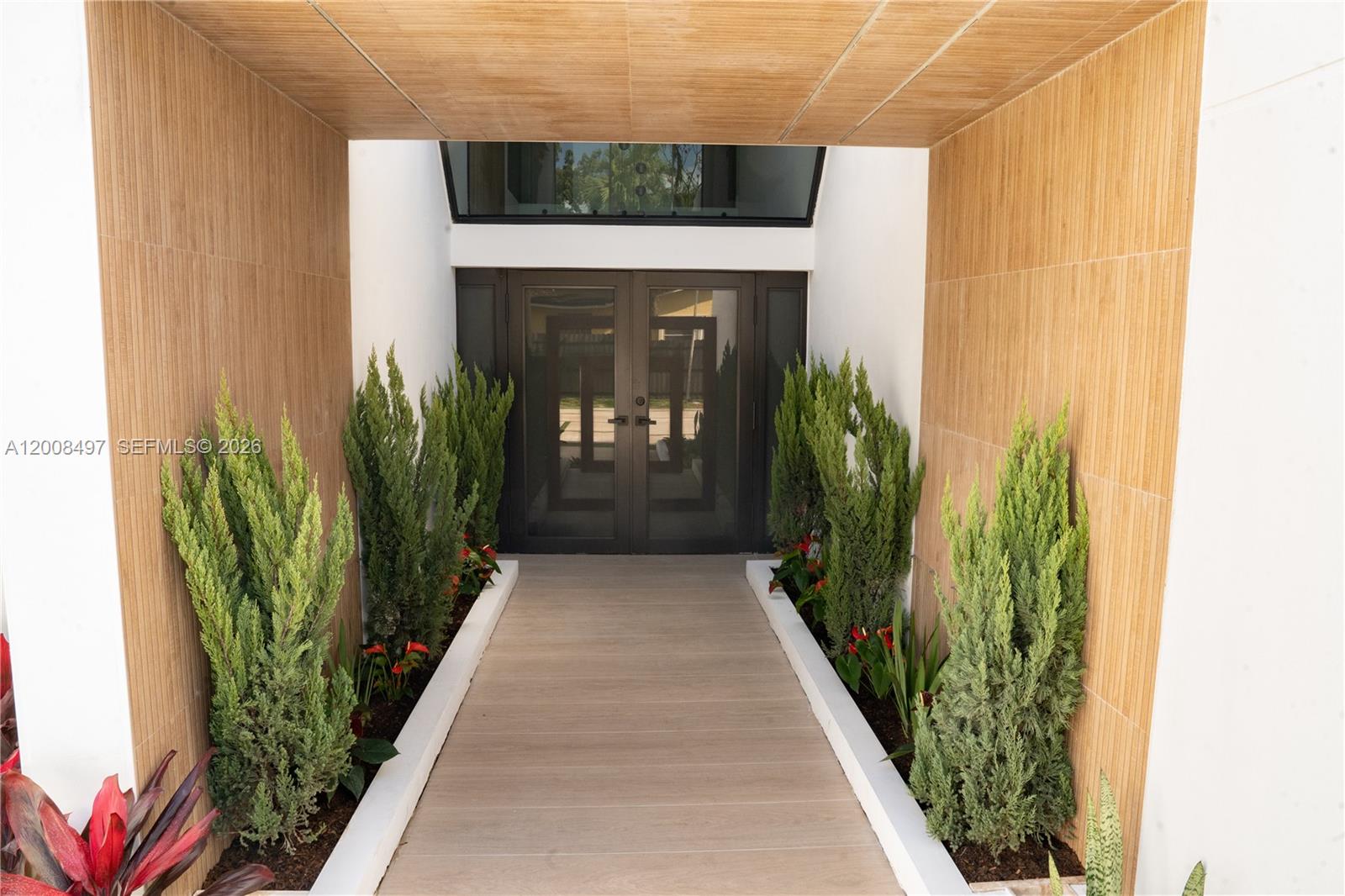 A wooden walkway leads to a double-door entrance flanked by potted plants and wood-paneled walls — 10475 SW 72nd Ave, Pinecrest FL 33156, PINECREST, FL