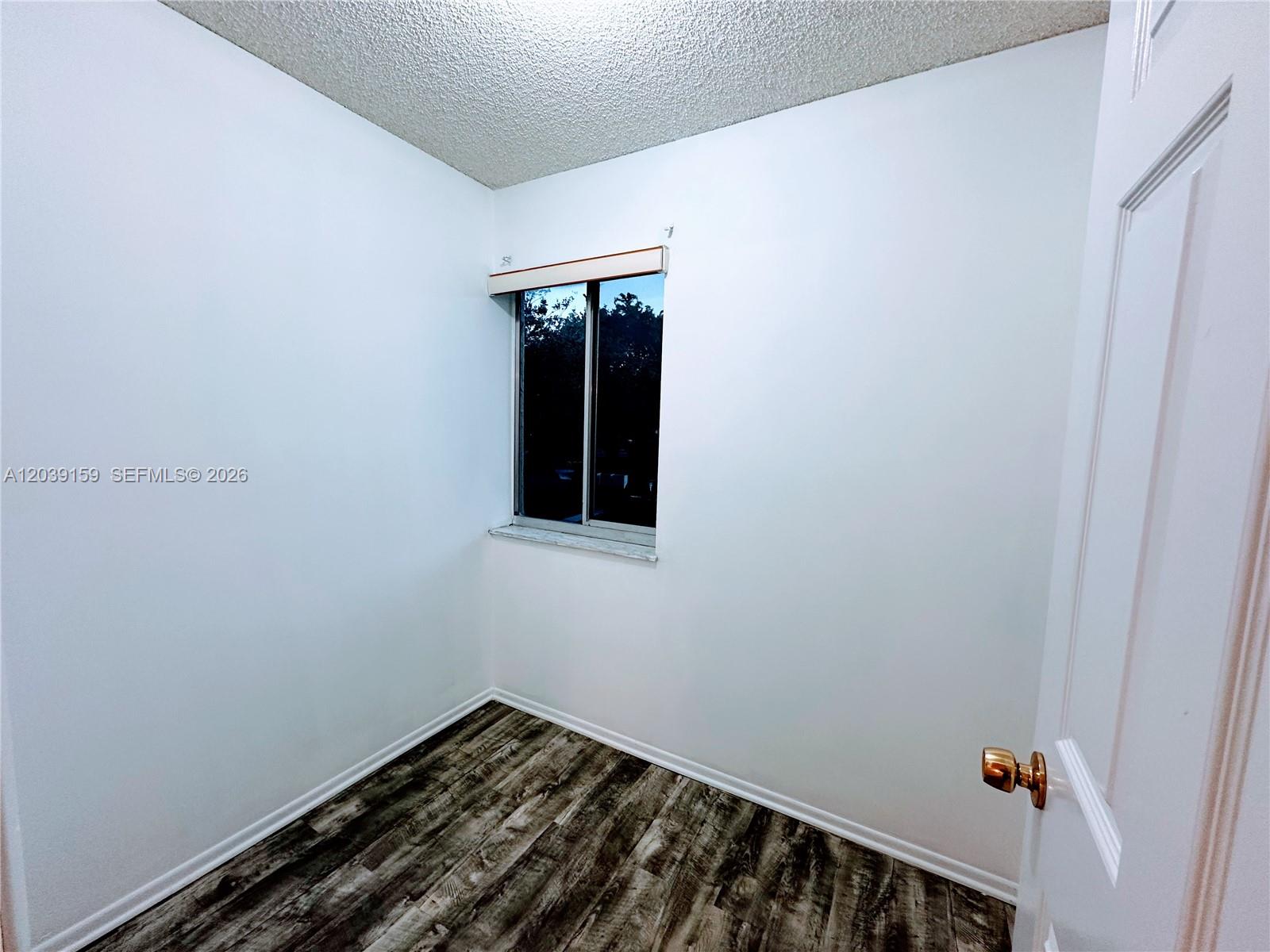A small, empty room features white walls, wood-look flooring, and a single window — 107 Gardens Dr # 205, Pompano Beach FL 33069, POMPANO BEACH, FL