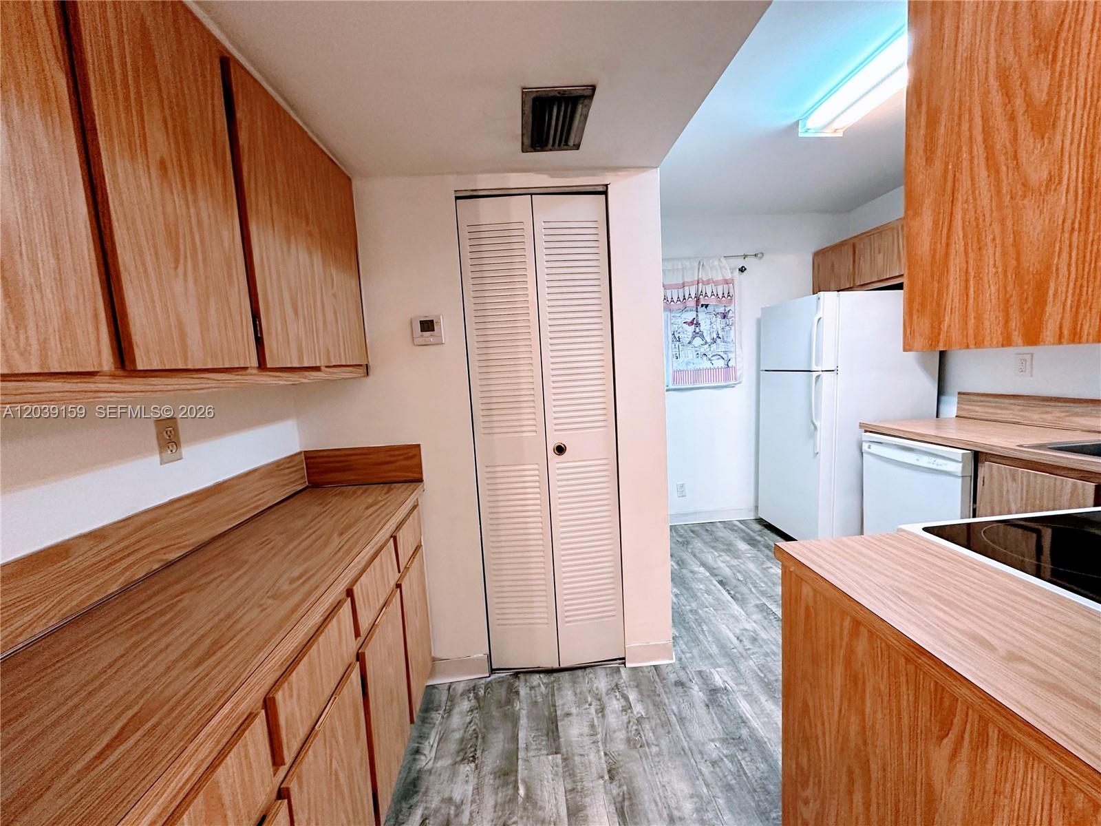 A kitchen features wood-grain cabinets, laminate countertops, and light-colored flooring — 107 Gardens Dr # 205, Pompano Beach FL 33069, POMPANO BEACH, FL