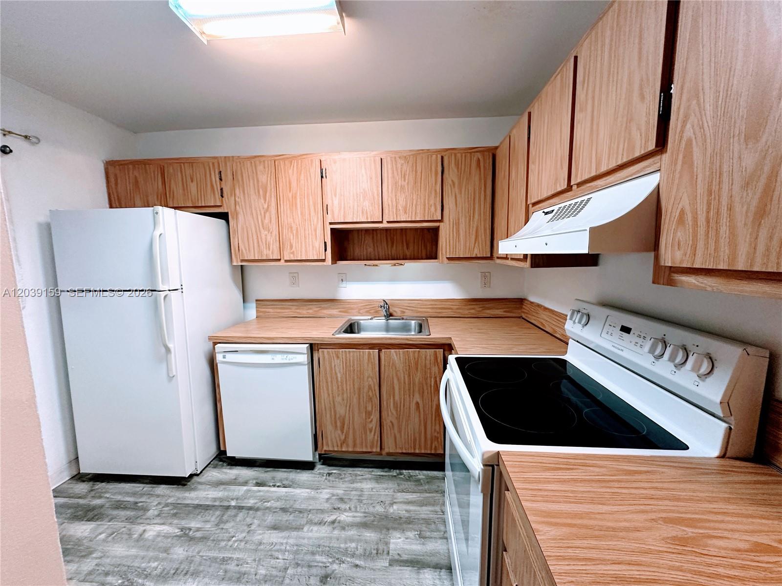 A kitchen features wood cabinets, white appliances, laminate countertops, and wood-look flooring — 107 Gardens Dr # 205, Pompano Beach FL 33069, POMPANO BEACH, FL