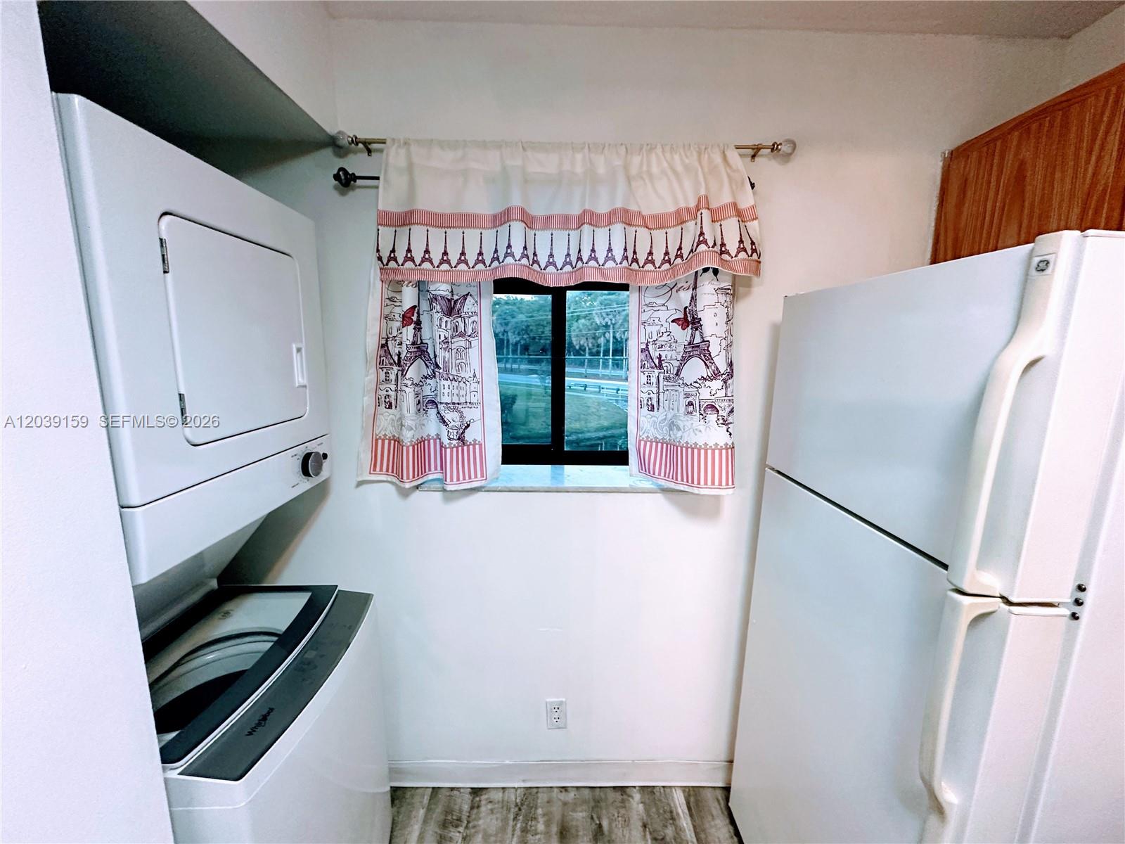 A laundry area features a stacked washer and dryer, a refrigerator, and a window — 107 Gardens Dr # 205, Pompano Beach FL 33069, POMPANO BEACH, FL