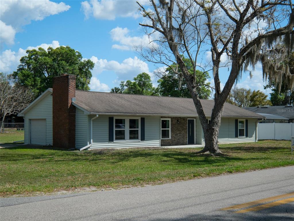 A single-story house with light siding, a brick chimney, and a large tree in front — 975 N BOSTON AVENUE, DELAND, FL