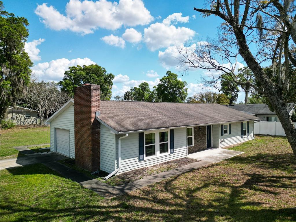 An exterior view of a single-story ranch house with white siding and a brick chimney — 975 N BOSTON AVENUE, DELAND, FL