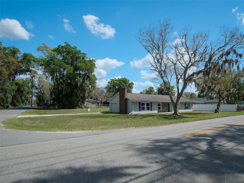 A single-story house with light siding and a brick chimney sits on a corner lot — 975 N BOSTON AVENUE, DELAND, FL