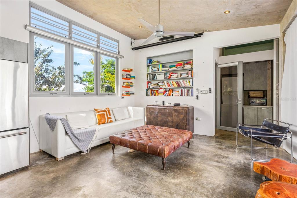 A modern living room features a white sofa, leather ottoman, built-in bookshelf, and concrete floors — PR 413 SOLAR C BO. PUNTAS, RINCON, PR
