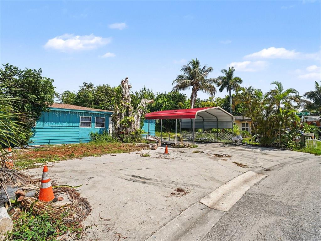 A turquoise house with a red-roofed carport sits on a gravel lot with palm trees — 2839 19TH STREET W, BRADENTON, FL