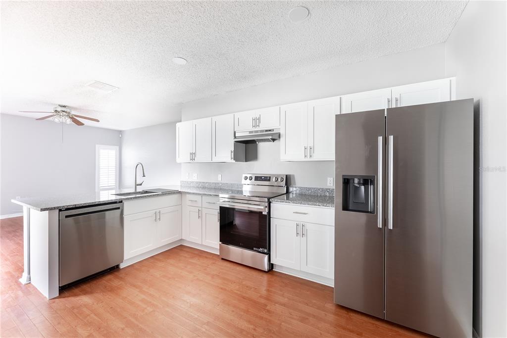 A kitchen features white cabinets, granite countertops, stainless steel appliances, and wood-look flooring — 234 BALBOA DRIVE, KISSIMMEE, FL