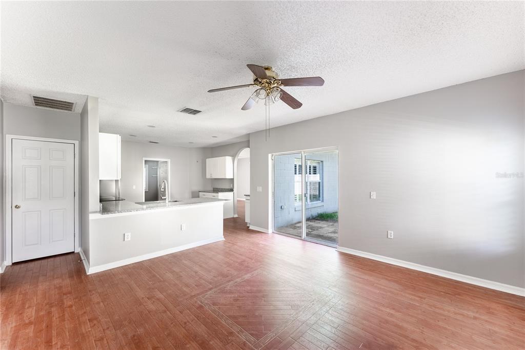 An open-concept living area features wood-look flooring, a kitchen island, and sliding glass patio doors — 234 BALBOA DRIVE, KISSIMMEE, FL