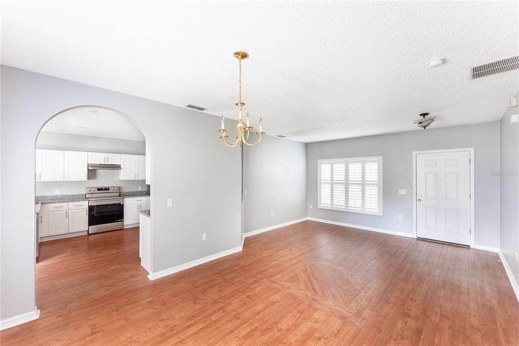An open dining area with wood-look flooring, a brass chandelier, and an arched kitchen entrance — 234 BALBOA DRIVE, KISSIMMEE, FL