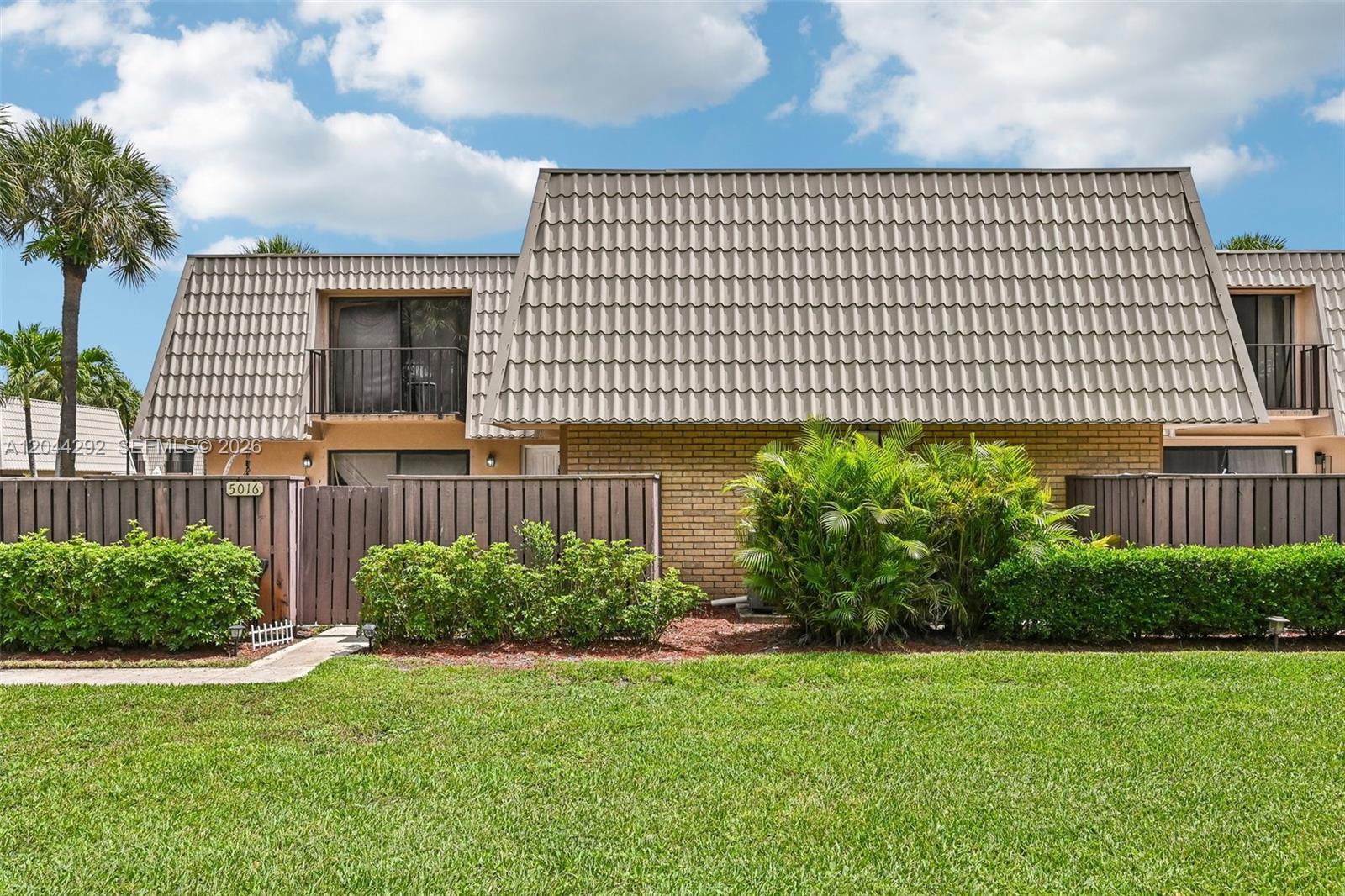 A two-story townhouse with a brown tiled mansard roof and a fenced-in front patio — 5016 50th Way, West Palm Beach FL 33409, WEST PALM BEACH, FL