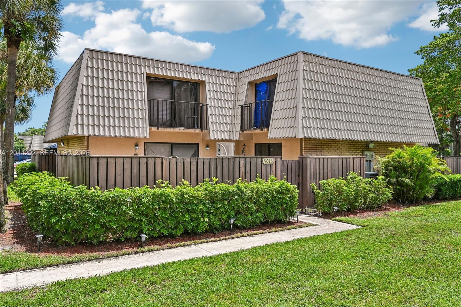 A two-story townhouse with a mansard roof, a wooden fence, and a manicured hedge — 5016 50th Way, West Palm Beach FL 33409, WEST PALM BEACH, FL