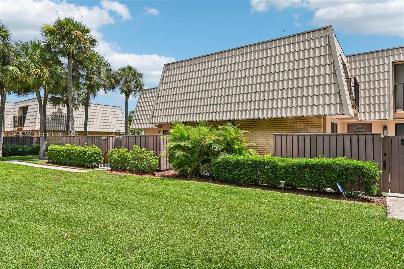 A view of a two-story townhouse exterior with a mansard roof, brick walls, and landscaping — 5016 50th Way, West Palm Beach FL 33409, WEST PALM BEACH, FL