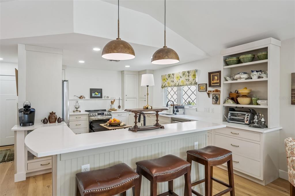 A kitchen features a white peninsula, leather bar stools, pendant lighting, and open shelving — 1304 SANTA ROSA COURT, THE VILLAGES, FL