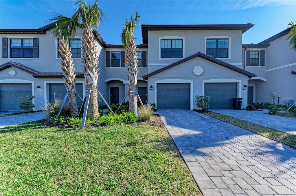 A two-story townhouse exterior features two garage doors, paved driveways, and two palm trees — 14713 LYLA TERRACE, BRADENTON, FL