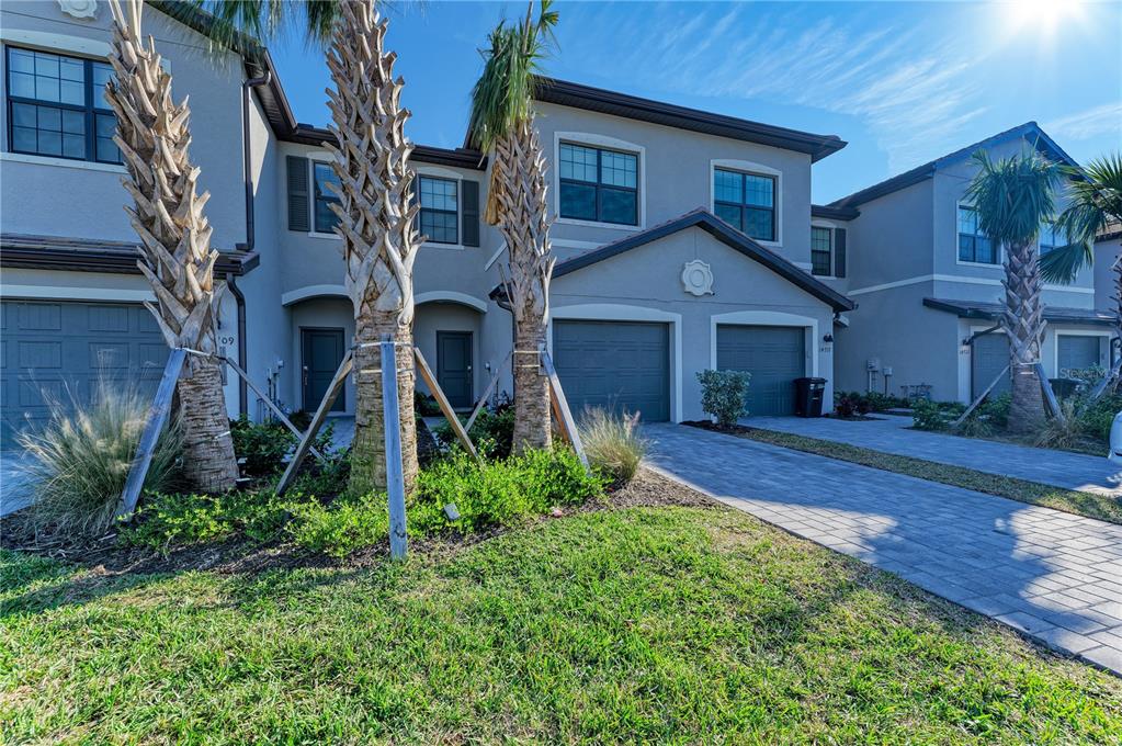A multi-story townhouse exterior with gray stucco, a paved driveway, and several palm trees — 14713 LYLA TERRACE, BRADENTON, FL