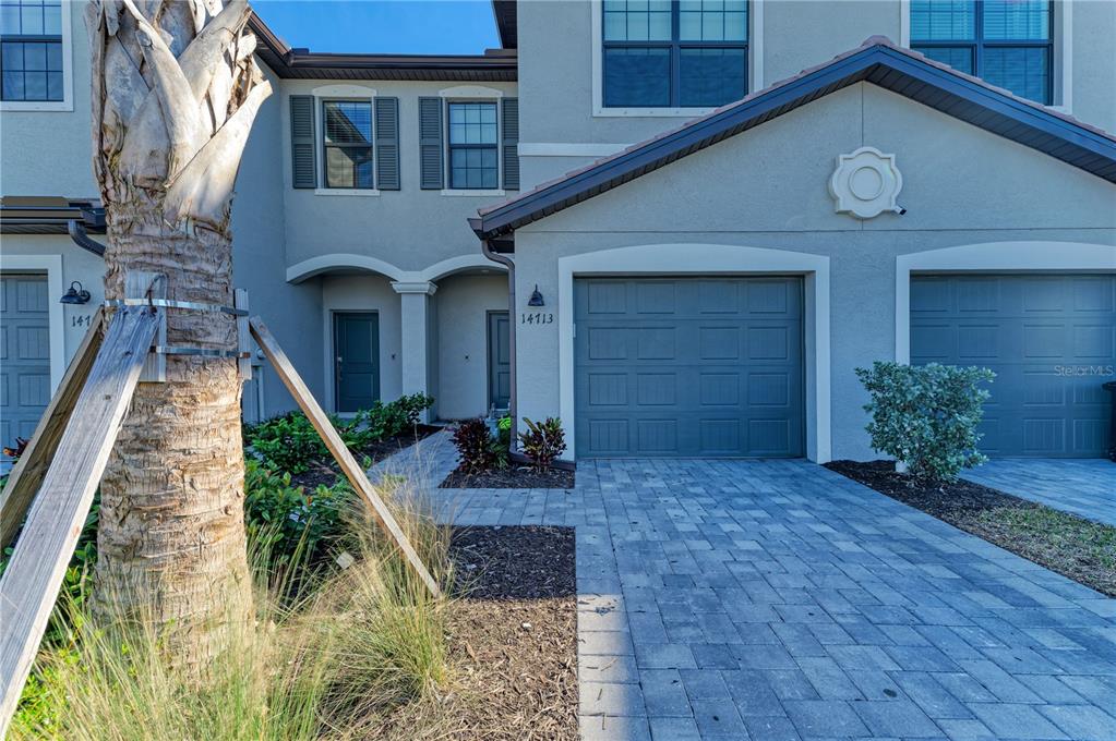A two-story townhouse exterior features a paved driveway, two garage doors, and a palm tree — 14713 LYLA TERRACE, BRADENTON, FL
