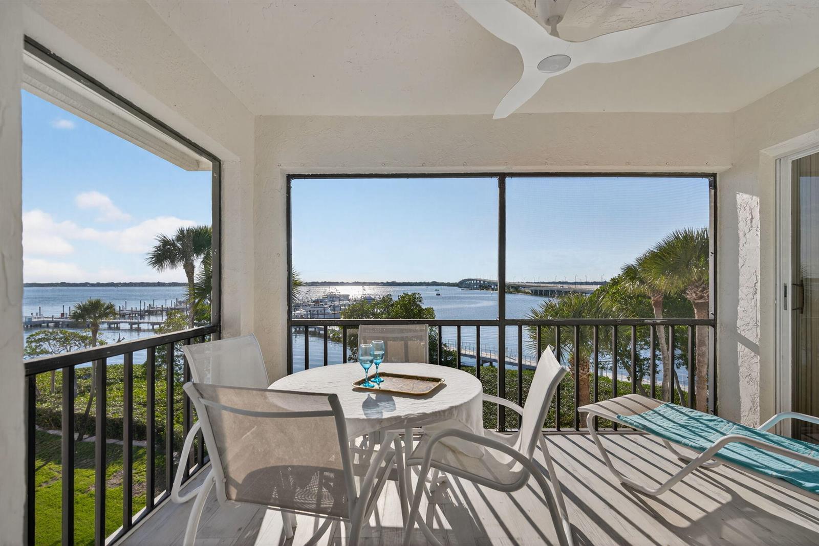A screened-in balcony features a dining set and lounge chair overlooking a bay and bridge — 390 NE Edgewater Drive # 403, Stuart FL 34996, STUART, FL