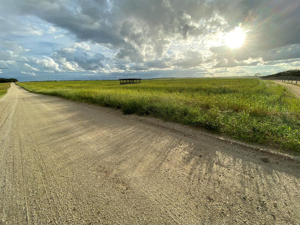 A dirt road runs alongside a large, grassy field under a cloudy, sunlit sky — 3700 SNYDER ROAD, SEBRING, FL