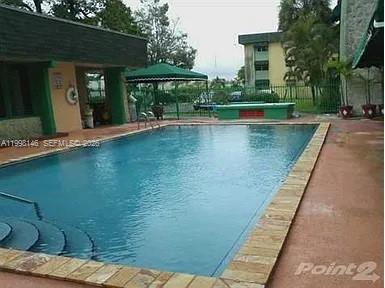 A rectangular swimming pool sits on a patio next to a building with green trim — 666 W 81st St # 124, Hialeah FL 33014, HIALEAH, FL