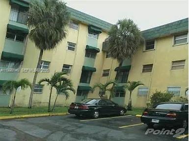 A low-rise apartment building with yellow stucco walls and green awnings stands above a parking lot — 666 W 81st St # 124, Hialeah FL 33014, HIALEAH, FL