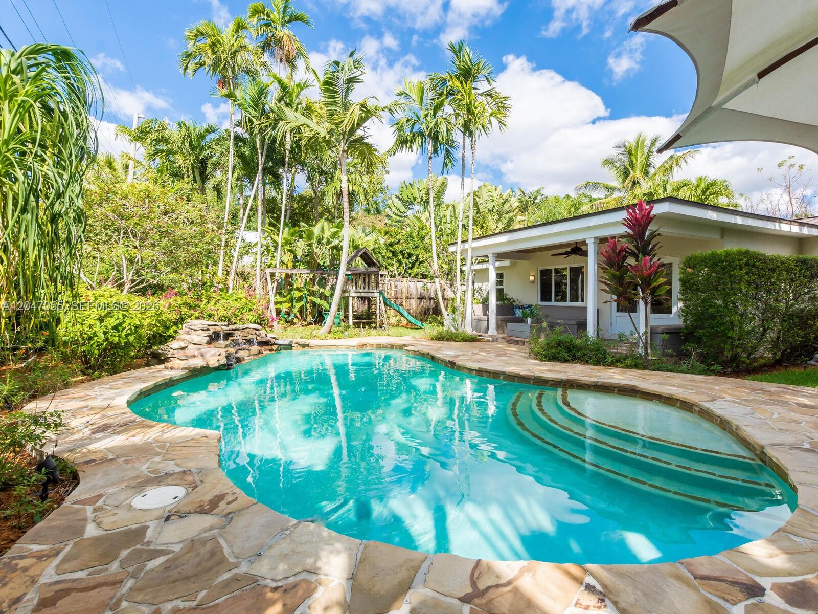 A backyard features a stone-paved pool with a waterfall next to a covered patio — 4054 Bonita Ave, Miami FL 33133, MIAMI, FL