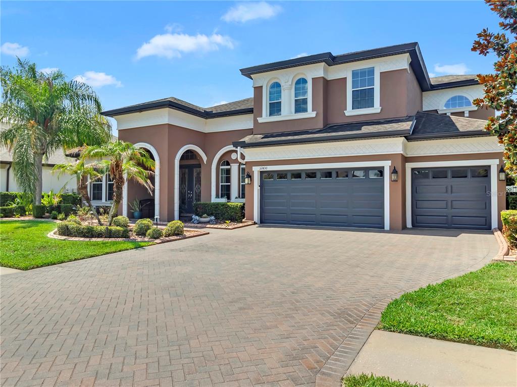 A two-story house with a brown stucco exterior, a brick paver driveway, and a three-car garage — 32430 SILVERCREEK WAY, WESLEY CHAPEL, FL