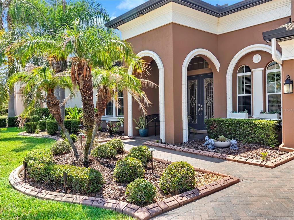The exterior of a brown stucco house features arched entryways, a brick walkway, and landscaping — 32430 SILVERCREEK WAY, WESLEY CHAPEL, FL