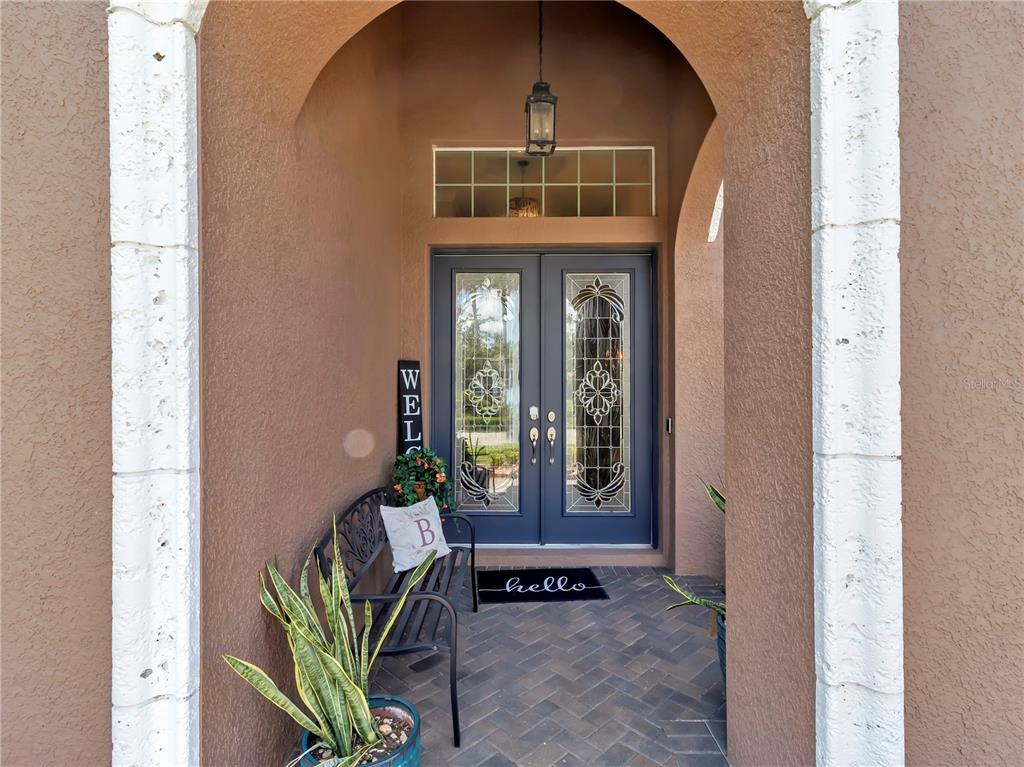 A covered entryway features a brick floor, a black metal bench, and double glass doors — 32430 SILVERCREEK WAY, WESLEY CHAPEL, FL